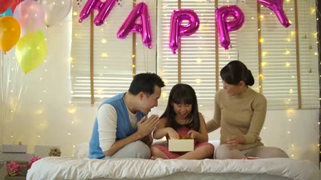 Familia-asiática-feliz-celebrando-el-cumpleaños-de-la-hija-de-apertura-regalos-y-se-regocijan-en-cama.-Navidad,-celebración-de-cumpleaños.-Fiesta-de-año-nuevo.-Cámara-lenta.