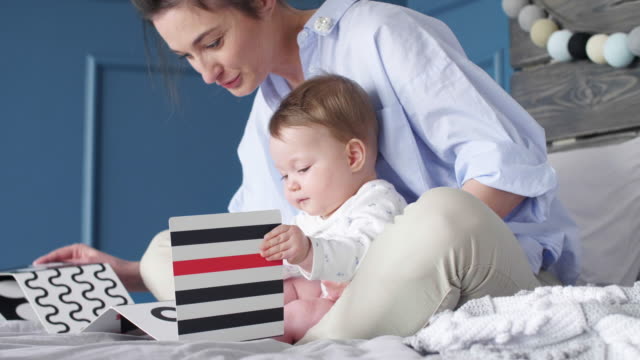 Junge-Mutter-und-Baby-beobachten-ein-Bilderbuch-im-Schlafzimmer
