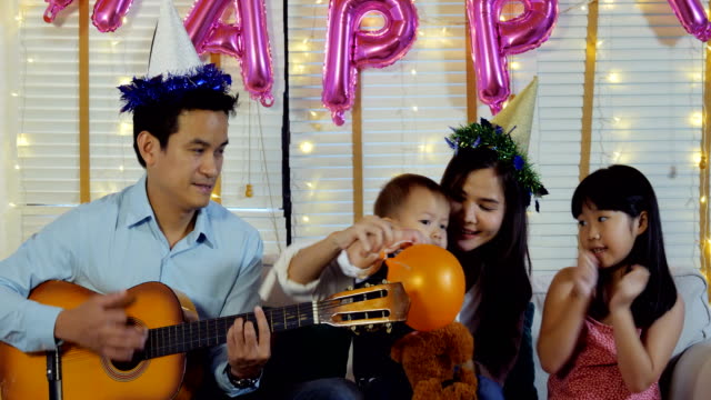 Father-playing-guitar-in-mini-party-at-home.-People-with-happy-family-and-party-concept.