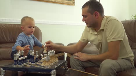 Joven-papá-jugando-al-ajedrez-con-su-pequeño-hijo