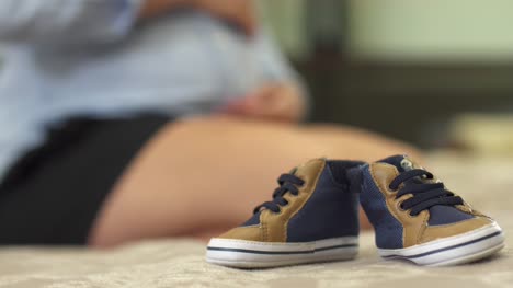 Kinder-Sneaker-auf-dem-Bett-neben-einem-schwangeren-Mädchen