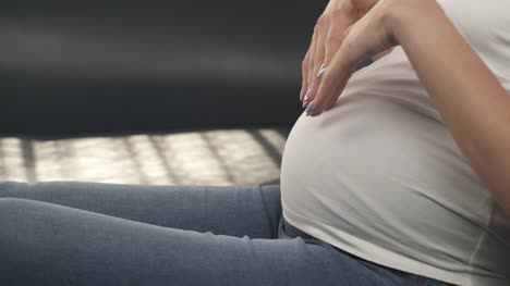 A-close-up-side-view-of-a-pregnant-woman's-belly.-Her-right-hand-slowly-starts-stroking-the-belly-and-then-she-makes-a-shape-with-both-hands-and-keeps-on-caressing-in-circles
