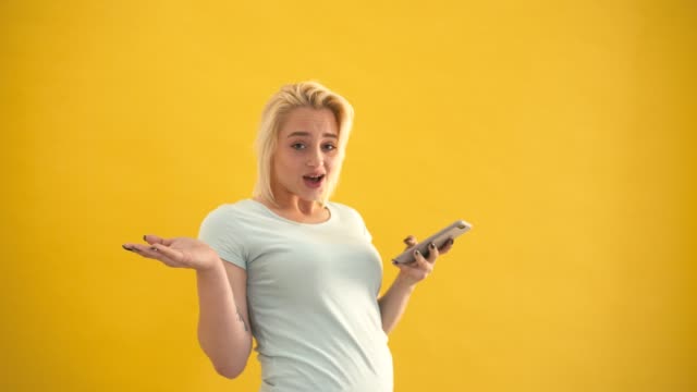 Unhappy-blond-plus-size-model-surprised-checking-message-on-phone-at-yellow-background