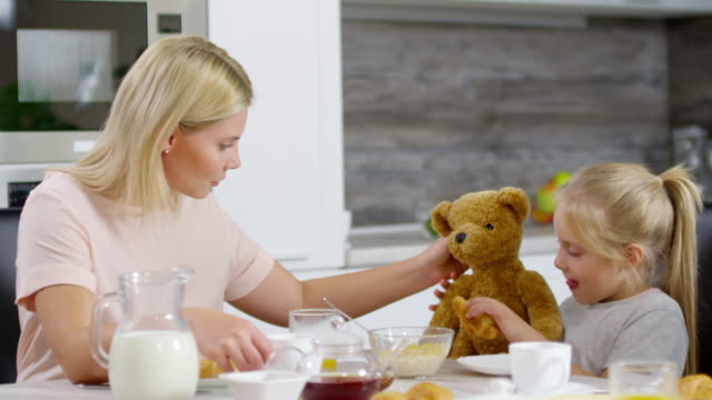 Kleine-Mädchen-und-Mama-füttern-tragen-Spielzeug-beim-Frühstück