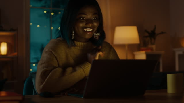 Porträt-von-schönen-lächelnden-schwarze-Mädchen-sitzt-an-ihrem-Schreibtisch-mit-Laptop,-einen-Videoanruf-tätigen-lässt-grüßen.-In-den-Abend-Mädchen-Gespräche-mit-Verwandten-und-Freunden-mit-Computer-Webcam.