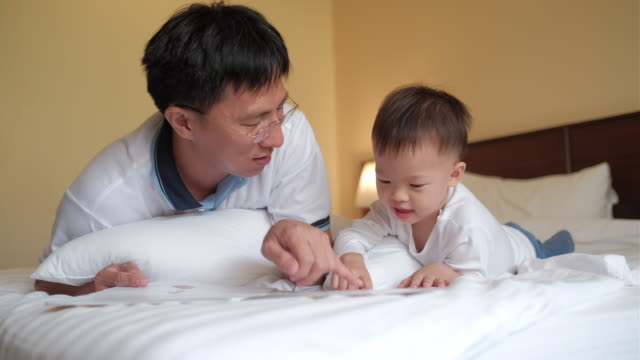 Asiático-padre-e-hijo-leyendo-historia-de-bedtime-del-libro-en-la-cama