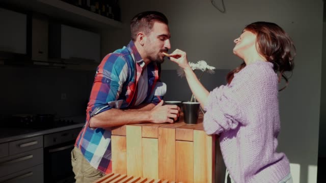 Woman-feeding-smiling-boyfriend-with-a-cookie-in-the-kitchen