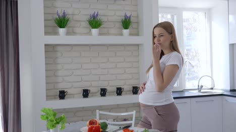 Schwangerschaft-und-gesunde-Ernährung,-schöne-Mädchen,-Gemüse-schneiden-und-Essen-Tomaten-mit-ihrem-großen-Bauch-in-Küche