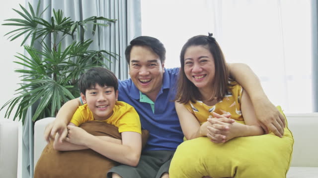 Lenta-de-asiático-familia-padre-madre-e-hijo-en-sofá,-mirando-a-cámara-con-sonrisa-cara.