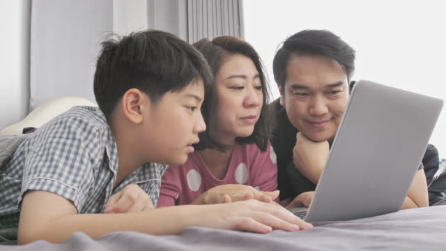 Feliz-familia-padre-madre-e-hijo-viendo-la-computadora-portátil-y-te-diviertes,-lenta-4K-Asia-resto-familiar-en-cama-con-el-ordenador-portátil