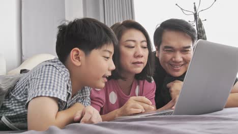 Happy-family-Father-mother-and-son-watching-on-laptop-computer-and-having-fun,-Slow-motion-4K--asian-family-rest-on-bed-with-laptop-computer