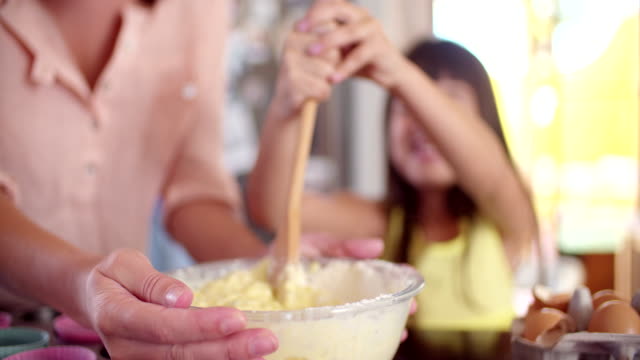 Niña-con-su-pastel-de-agitación-ingredientes-Niña-feliz-pastel-de-agitación-ingredientes-en-un-plato-con-una-cuchara-de-madera-con-su-madre-en-sus-kitchenmom