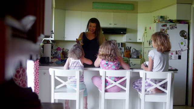 A-mother-talks-to-her-daughters-at-the-kitchen-counter-in-the-morning