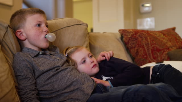 Junge-Geschwister-sitzen-nahe-beieinander-auf-der-Couch-und-vor-dem-Fernseher