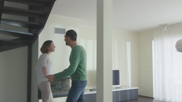 Happy-couple-are-walking-into-a-new-home-and-looking-around-the-apartment.
