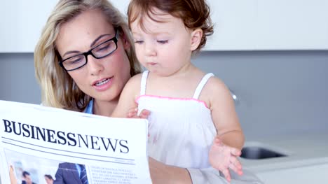 Blonde-Mutter-lesen-Zeitung-mit-ihrem-Baby-zu-schärfen