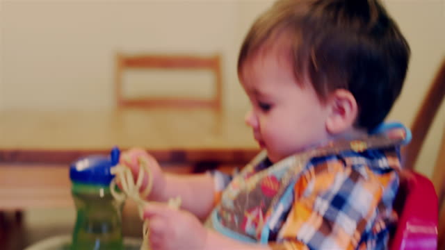 Entzückende-Baby-Junge-sitzt-in-einem-Hochstuhl-Booster-Sitz-und-essen-Spaghetti-mit-seinen-Händen