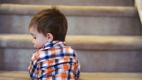Little-boy-standing-at-the-bottom-of-stairs,-holding-a-sippy-cup