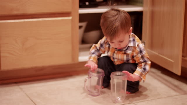 Pequeño-niño-apilando-plasticware-en-el-piso-de-la-cocina