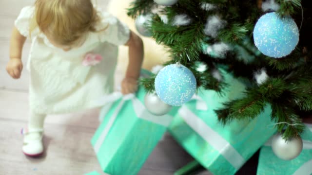 Süßes-Babymädchen-nimmt-ihr-Geschenk-unter-Weihnachten-Tre-und-geht-auf-ihre-junge-Mutter
