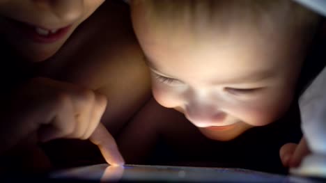 Dos-hermanos-jóvenes-jugando-con-tabletas-por-la-noche.-4K