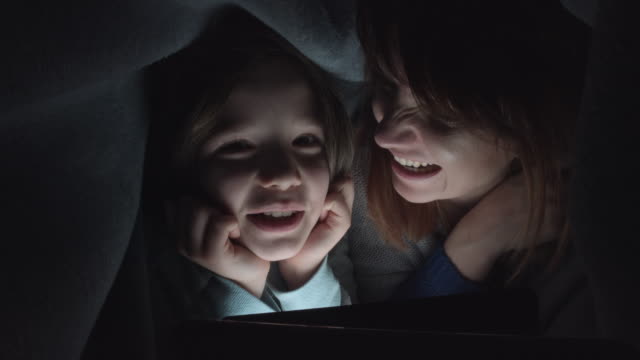 4k-Shot-of-Child-and-Mom-Looking-on-Tablet-under-Blanket