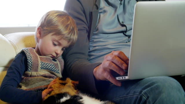 moderne-Familie-kleines-Mädchen-spielt-mit-Katze-während-Papa-arbeitet-mit-Notebook-auf-Couch-indoor-in-modernen-industriellen-Haus.-Kaukasische.-4k-handheld-nahaufnahme-Slow-Motion-video-gedreht