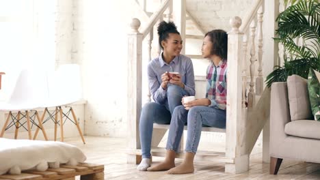 Zwei-afrikanische-amerikanische-lockige-Mädchen-Sistres-sitzen-auf-Treppen-haben-Spaß-lachen-und-chatten-zusammen-zu-Hause