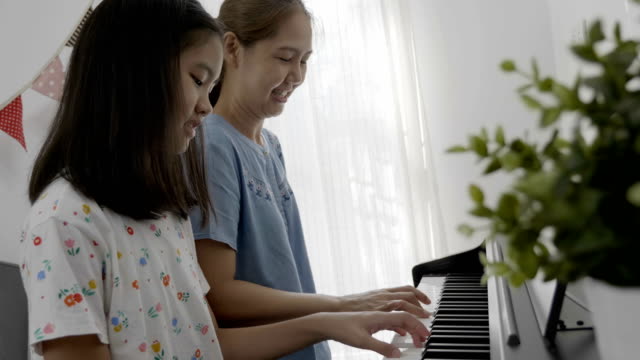 4K:-asiatische-Mutter-spielt-Klavier-mit-Tochter-zu-Hause-glücklich
