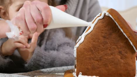 Die-Frau-legt-eine-weiße-Creme-auf-ein-Lebkuchenhaus