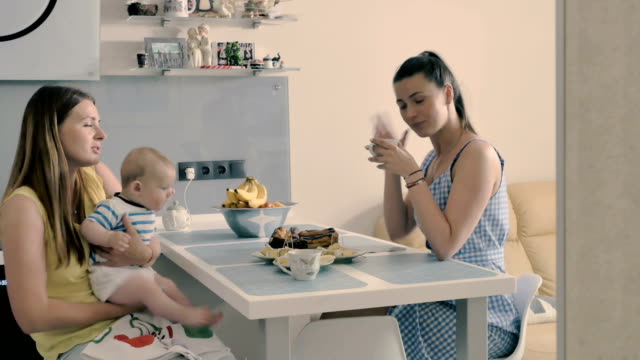Junge-Mutter-mit-Baby-trinkt-einen-Tee-mit-ihrer-Freundin-in-der-Küche-zu-Hause