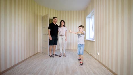 Happy-family-walking-in-new-house.-Joyful-boy-opening-door-entering-his-room-for-the-first-time.-Mother-father-and-son-standing-inside-of-their-modern-apartment-discussing-future-interior