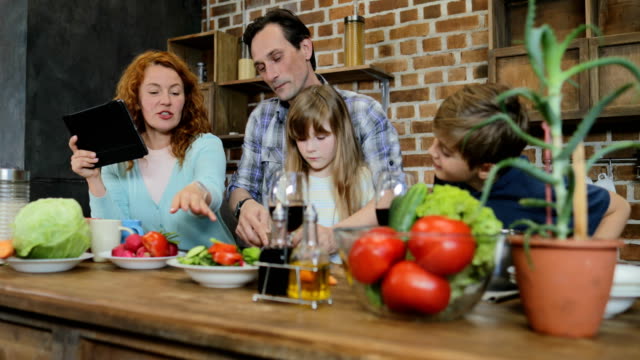 Vater-und-Tochter-Hacken-Gemüse-kochen-zusammen-In-der-Küche,-im-Gespräch-mit-Sohn-und-Mutter-mit-Tablet-Digitalrechner-glückliche-Familie-zu-Hause-zu-kommunizieren