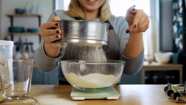 Close-up-view-of-young-beautiful-woman-weighs-the-flour-using-kitchen-scales,-bowl-and-sieve-for-this