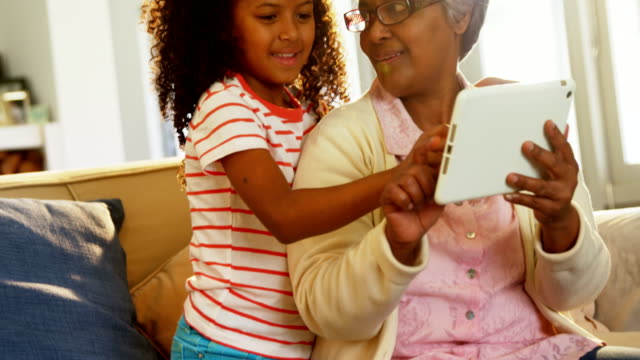 Lächelnden-Großmutter-und-Enkelin-mit-digital-Tablette-auf-Sofa-im-Wohnzimmer-4k
