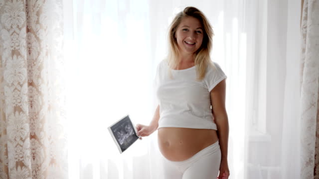 maternidad,-mujer-expectante-muestra-a-infantil-de-exploración-de-ultrasonido-en-la-cámara-cerca-del-vientre