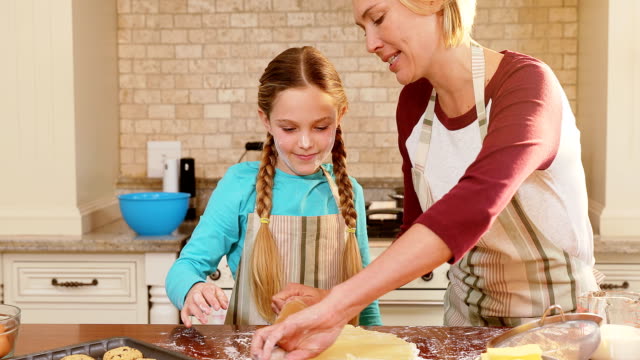 Smiling-mother-and-daughter-wearing-apron-rolling-dough-together-4K-4k