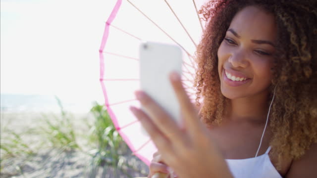 Mujer-afroamericana-con-teléfono-inteligente-en-la-playa