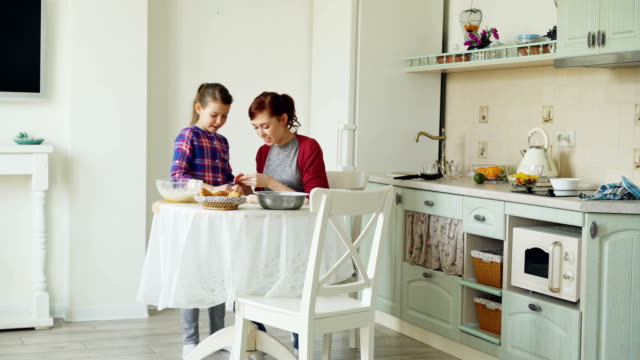 Lächelnde-Mutter-und-niedliche-Tochter-machen-Cookies-zusammen-mit-Teig-während-der-Sitzung-in-der-modernen-Küche-zu-Hause.-Familie,-Essen-und-Leute-Konzept