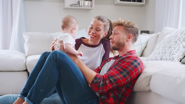 Young-white-couple-sit-playing-with-baby-at-home,-side-view