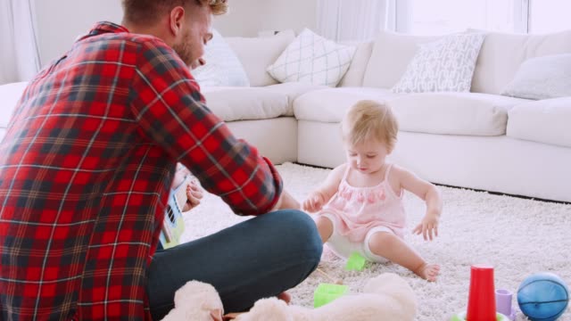 Young-dad-playing-ukulele-with-toddler-girl-in-sitting-room