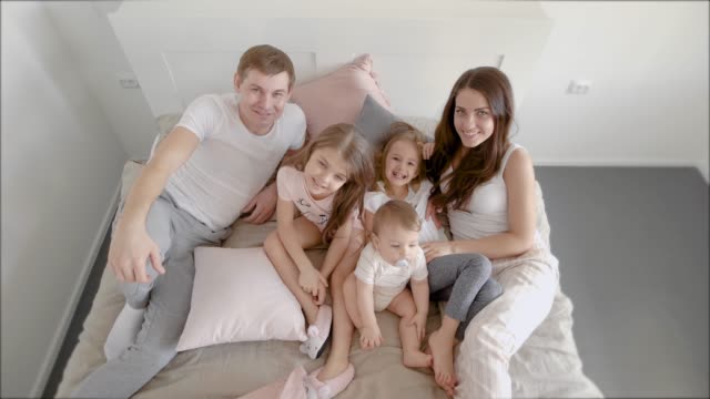 a-portrait-of-a-young-and-friendly-family-who-are-in-their-cozy-bedroom-on-the-bed,-a-large-mother-and-a-happy-head-of-the-family