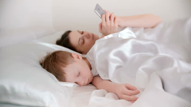 Mutter-wachte-auf-und-Surfen-im-Internet-in-ihr-Handy-während-ihres-Sohnes-noch-schläft.