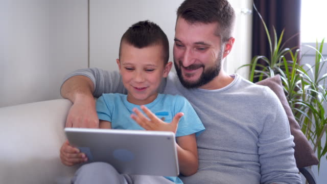 Smiling-father-and-son-using-tablet-while-sitting-on-sofa