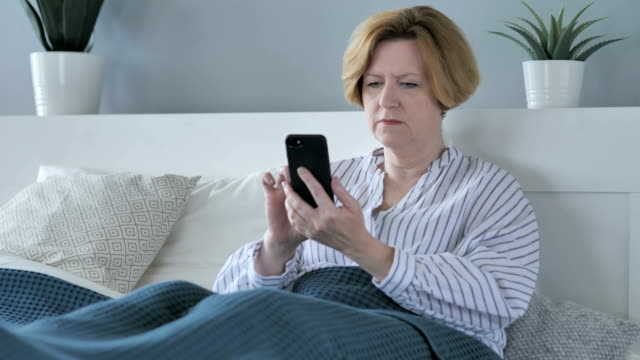 Alten-Senior-Frau-mittels-Smartphone-beim-liegen-im-Bett