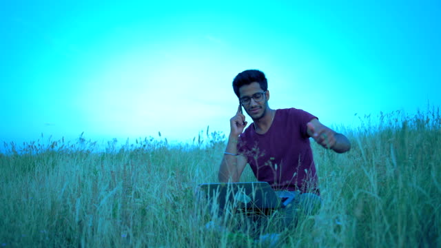 Indischen-Mann-in-der-Brille-Spaß-Kommunikation-am-Telefon-sitzen-auf-dem-Rasen-auf-dem-Hügel-am-Abend