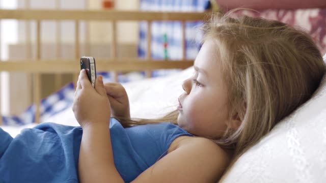 Kleines-Mädchen-auf-dem-Bett-liegend-und-mit-smartphone