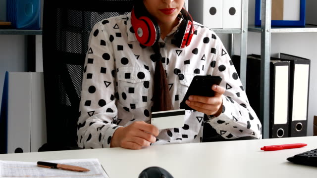 Frau-mit-roten-Kopfhörer-auf-Schultern-halten-Kreditkarte-und-mit-smartphone