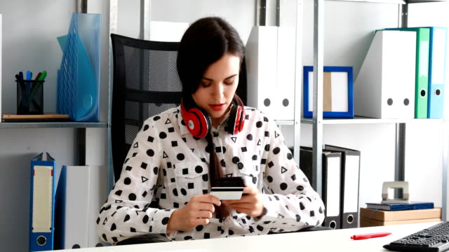 woman-with-red-headphones-on-shoulders-entering-credit-card-number-into-smartphone