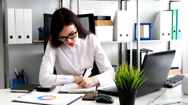 businesswoman-filling-documents-and-working-on-laptop-in-modern-office